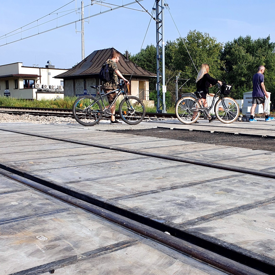 Zdjęcie przedstawia przechodzących rowerzystów na nowo zmodernizowanym przejeździe kolejowo-drogowym na ulicy Półłanki w Krakowie.